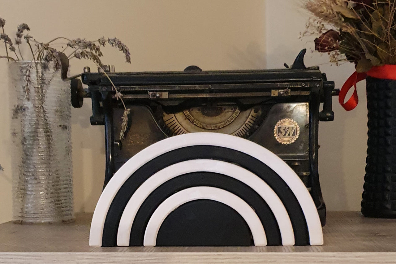 A six-piece black and white Waldorf stacker placed on a wooden surface with a vintage typewriter and dried floral decor in the background.