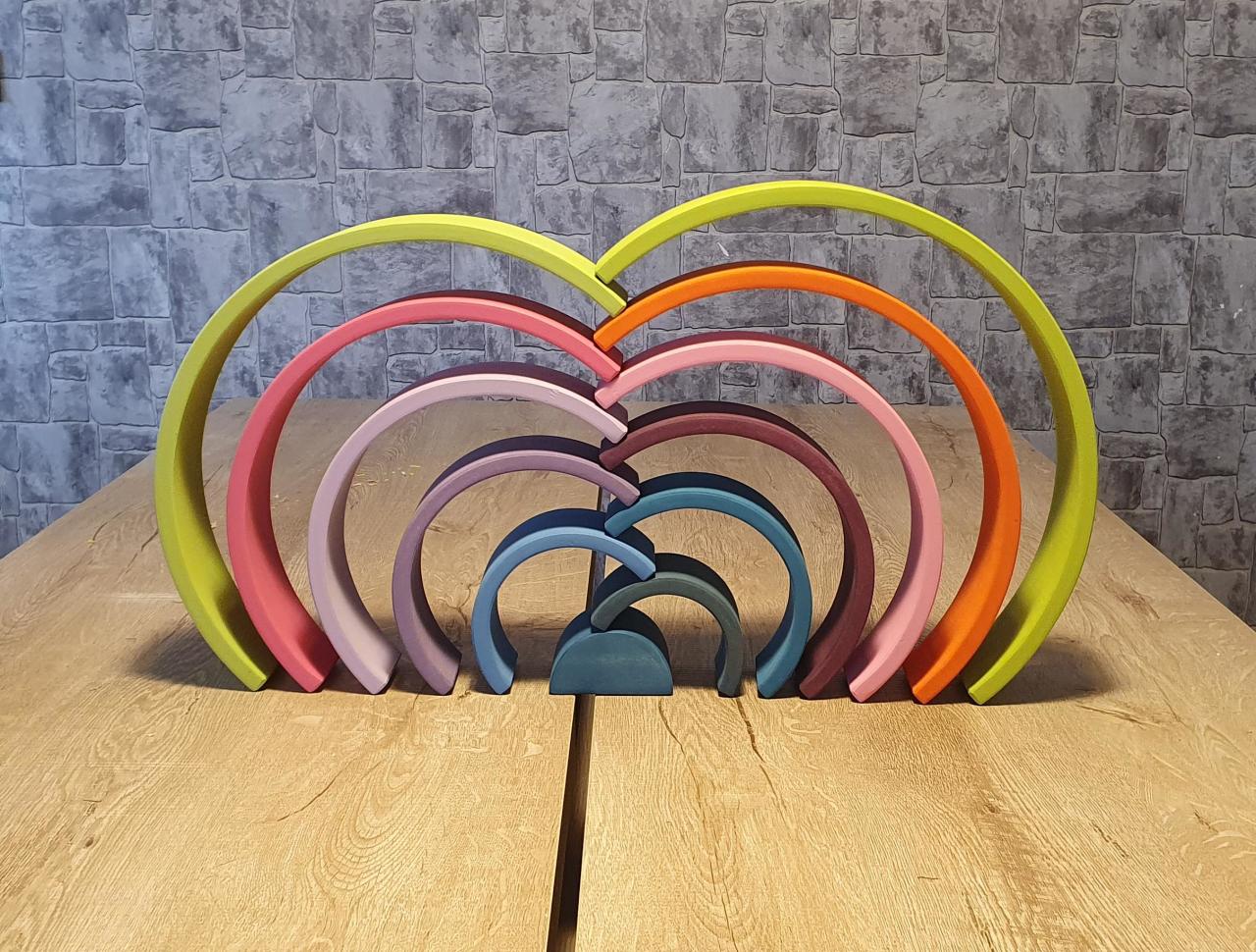 Pastel Waldorf rainbow stacker arranged in an arched design on a wooden table with a textured wall in the background.