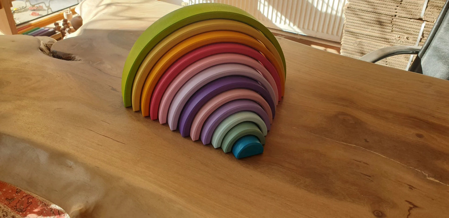 Waldorf rainbow stacker toy arranged on a wooden table in natural sunlight.
