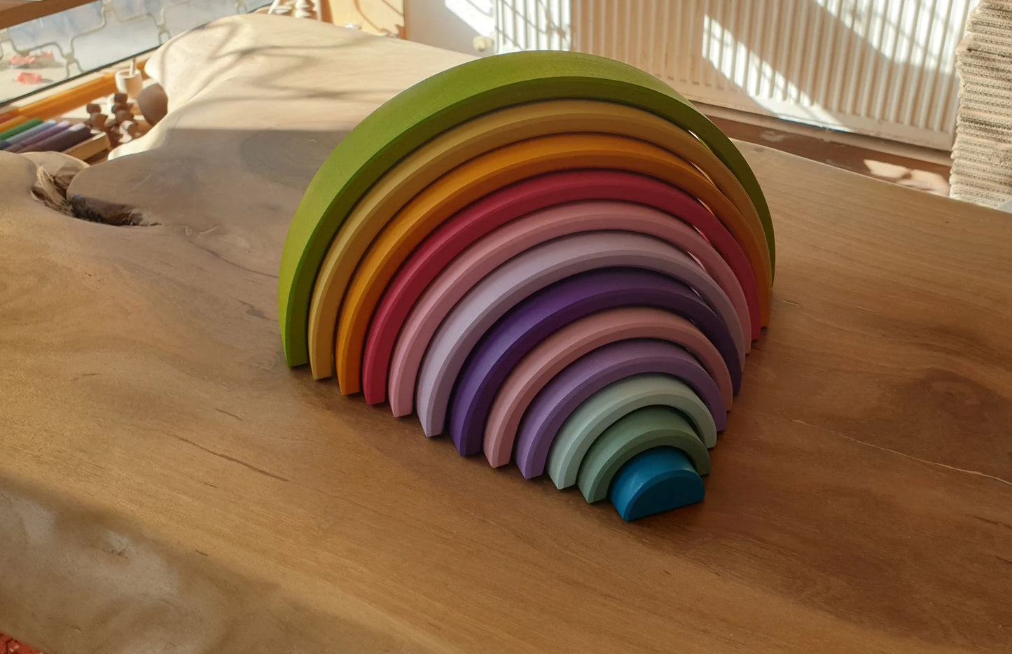 Colorful Waldorf rainbow stacker toy displayed on a natural wooden table in a sunlit room.
