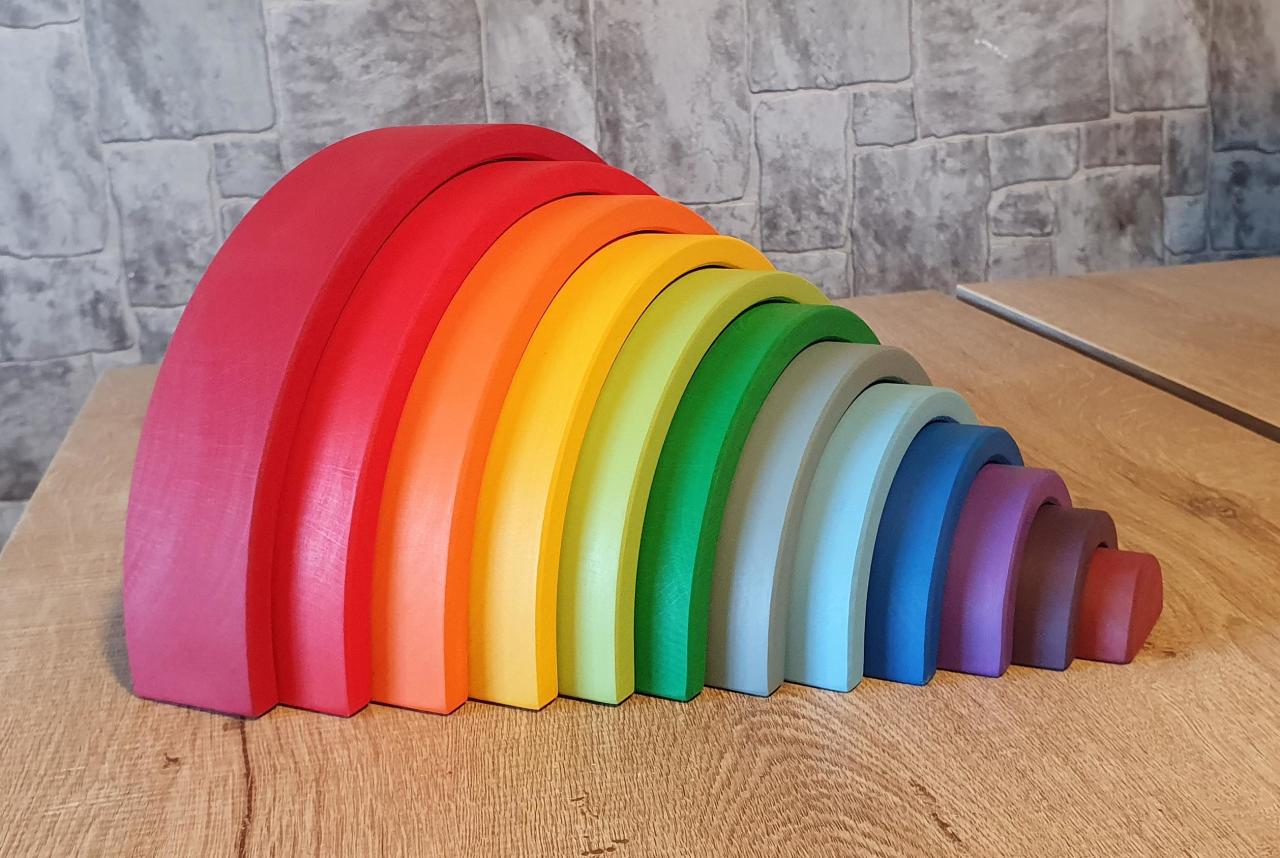 Waldorf rainbow stacker toy arranged side by side on a wooden table, showcasing its gradient of vibrant colors from red to violet.